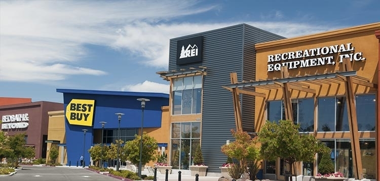 Exterior view of a well-maintained modern shopping center featuring Recreational Equipment, Inc, Best Buy, and Bed Bath & Beyond.
